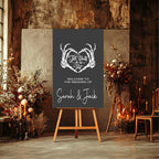A personalized wedding sign on a wooden easel in a rustic, candle-lit venue. The sign is dark charcoal gray with a white graphic of skeletal hands forming a heart and the text 'I'll Never Love Without You' and 'WELCOME TO THE WEDDING OF Sarah & Jack'.