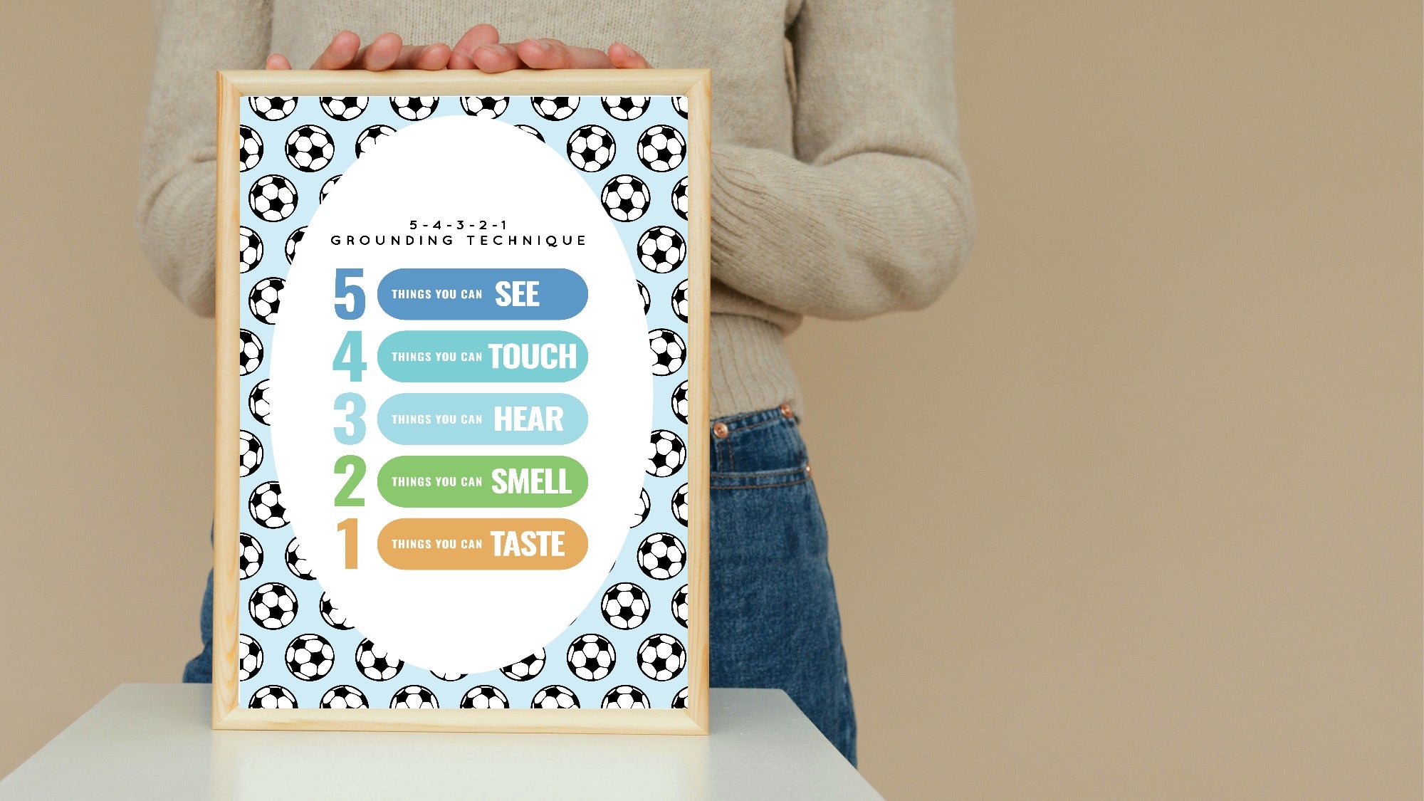 Person holding a framed poster with a five-sense grounding technique diagram on a beige background