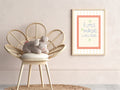 Wicker chair with a cushion and knitted toy, framed artwork on the wall.