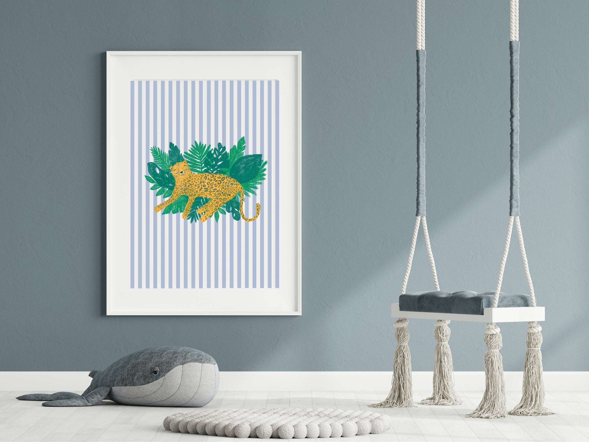 Framed artwork with a gold lion and green leaves on a blue striped background, hanging above a gray plush toy and small table.