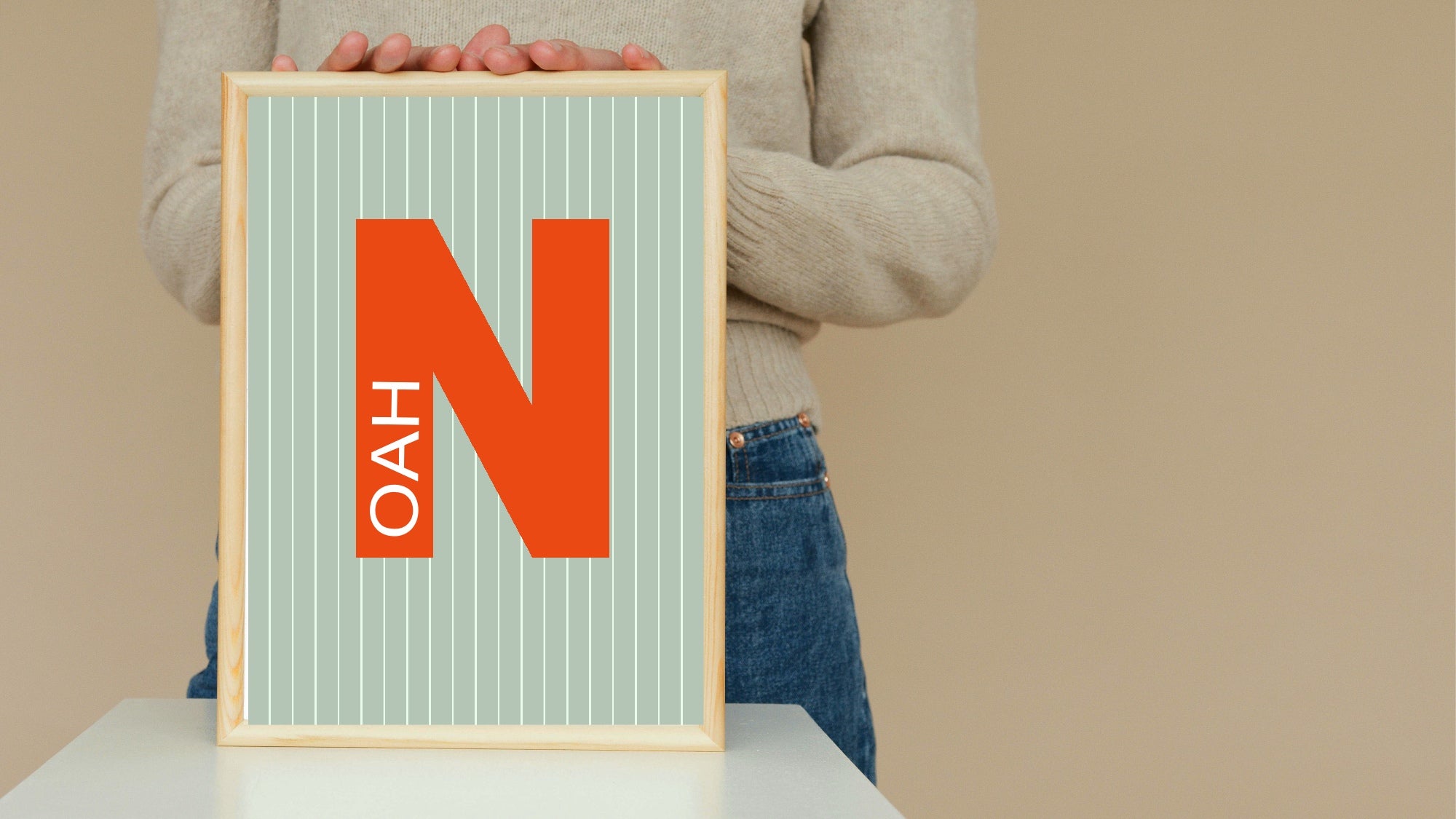 Person holding a framed poster with the letter 'N' and text on a beige background