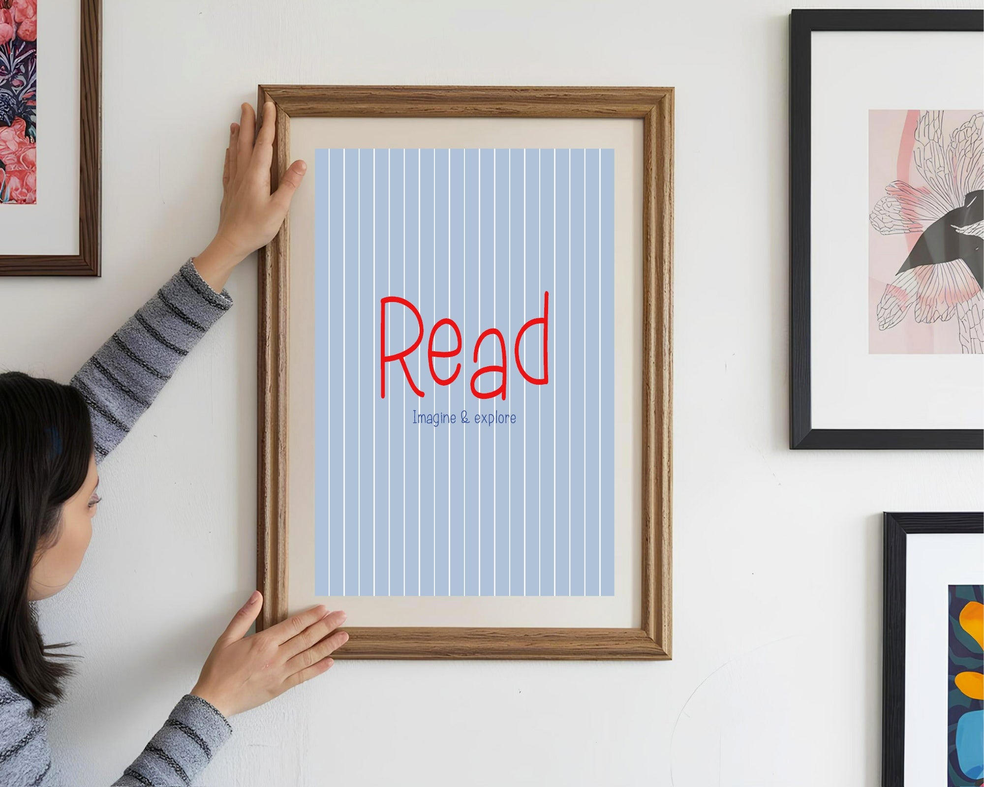 Person hanging a framed poster with 'Read' on a wall with other framed artworks.