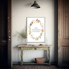 A framed art print with a floral wreath and the text 'COME IN. TAKE YOUR WELLINGS OFF & PUT YOUR HEET IN' hangs on a light wall above a distressed green console table in a rustic room.