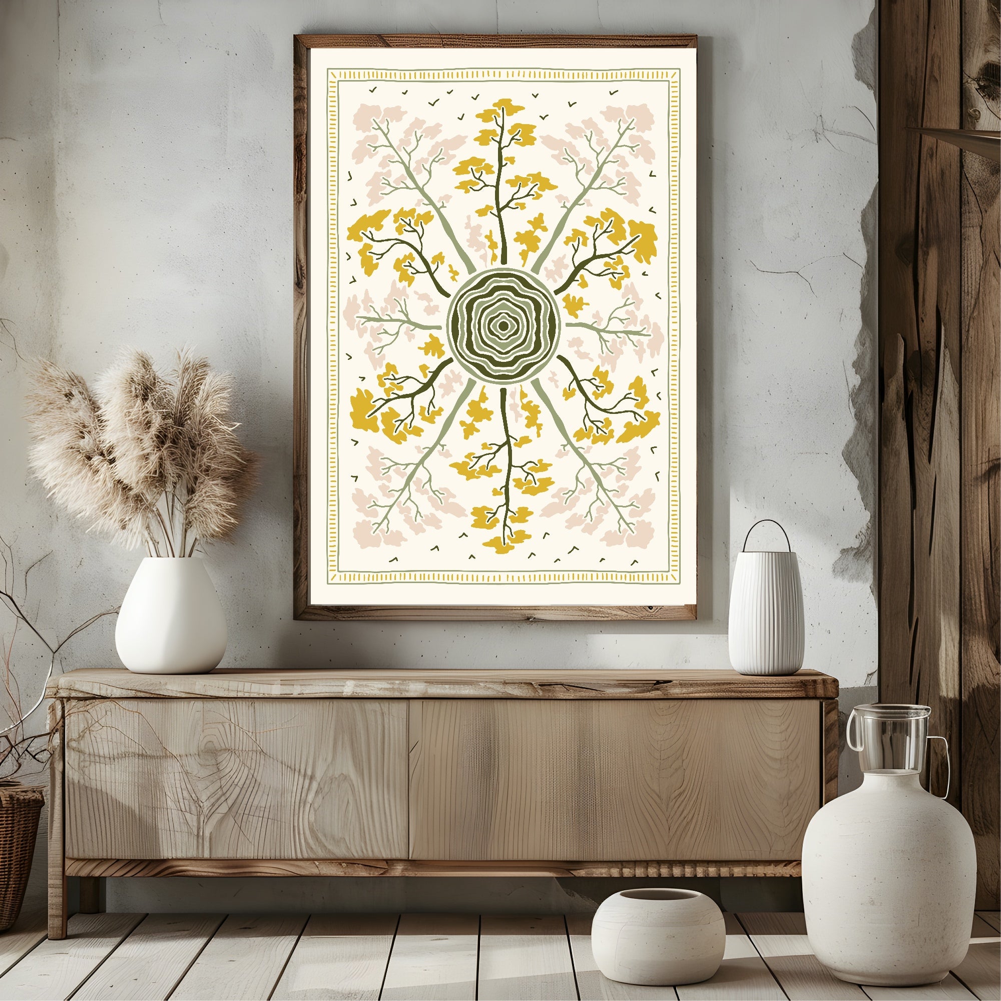 A framed botanical art print with a radial mandala design in yellow, olive green, and blush pink, displayed on a rustic wooden console table in a styled room setting.