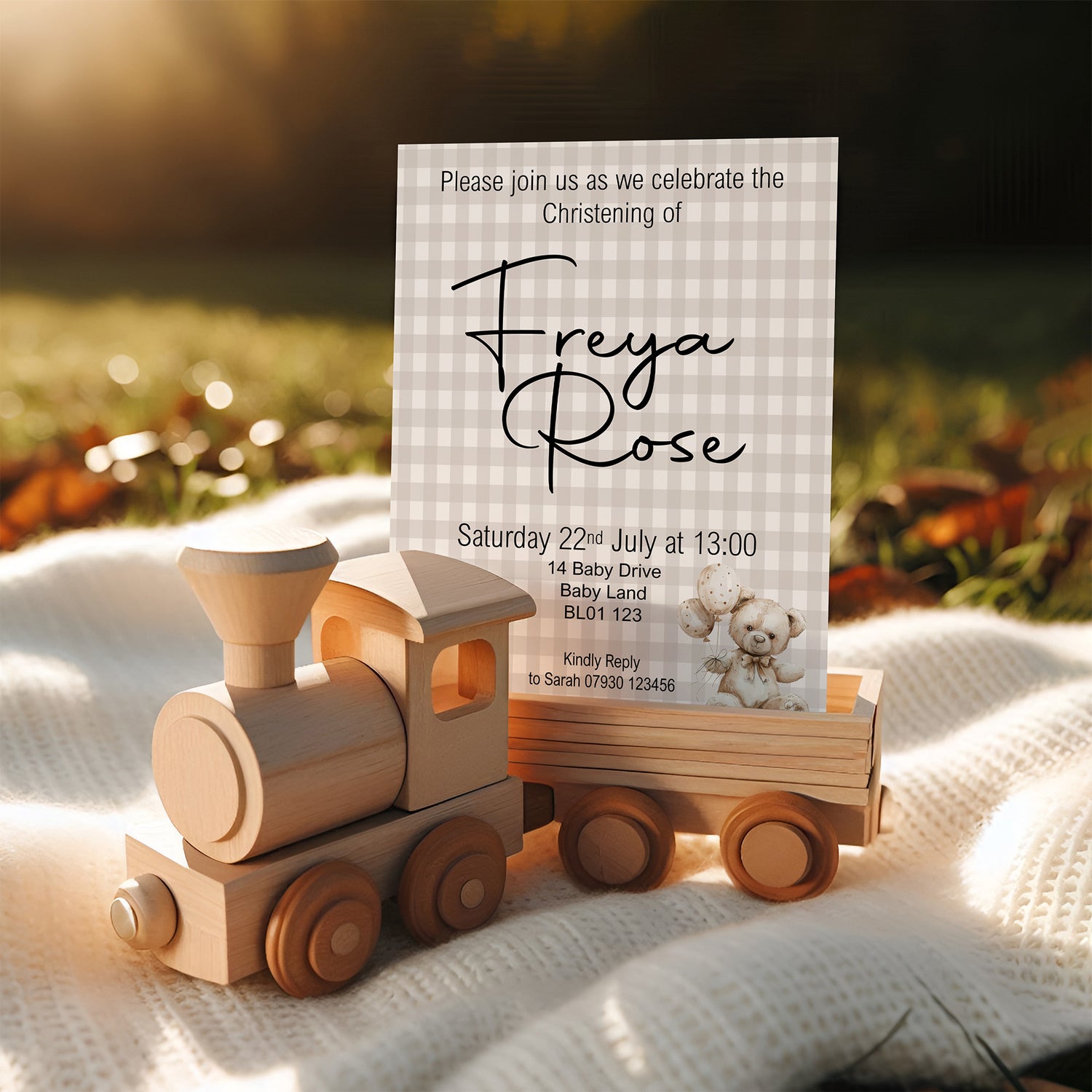 Wooden toy train with a Christening invitation card on a soft surface with a blurred natural background