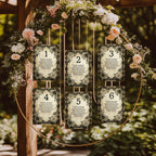 A floral arch with six hanging rectangular table number cards numbered 1 through 6, displayed outdoors on a wooden structure with greenery and pink flowers in the background.