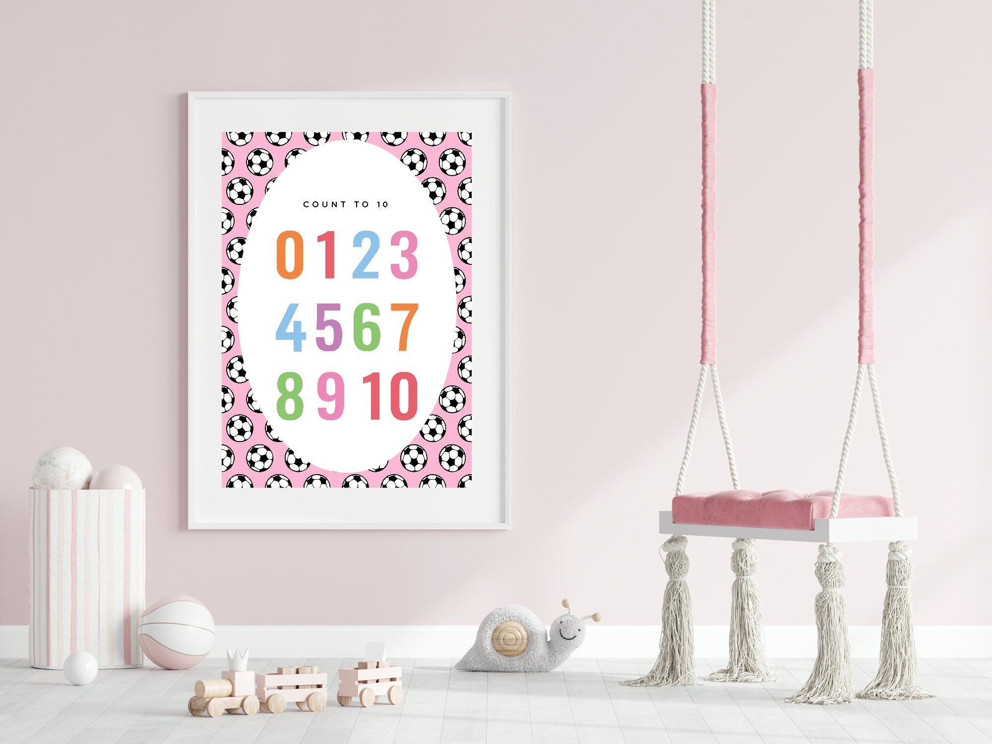 Framed children's poster with numbers and soccer ball pattern on a pink wall with a swing in the background.