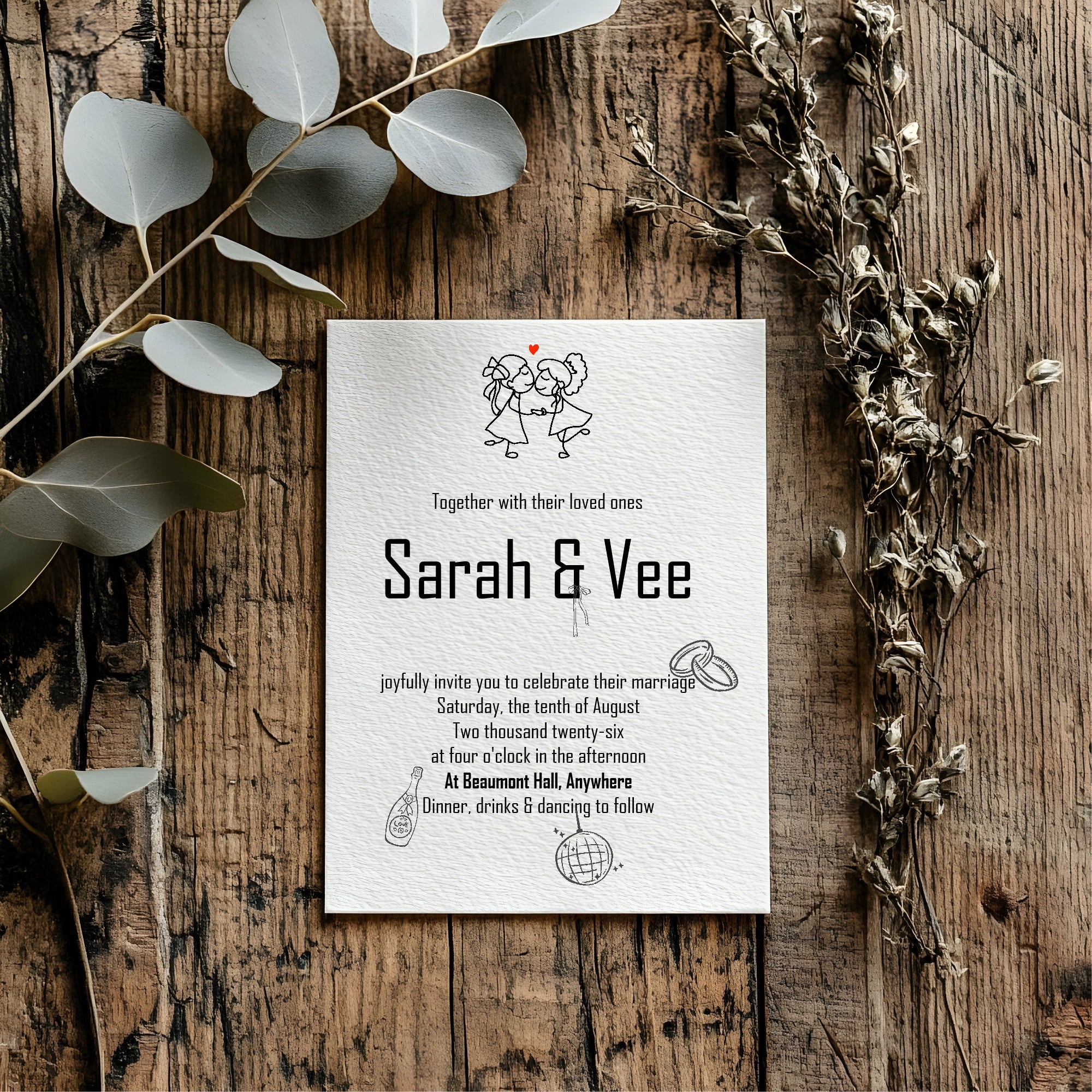 Wedding invitation card for Sarah & Vee on a wooden surface with decorative leaves.
