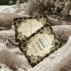 Vintage-style wedding invitation with black floral design on a lace fabric background