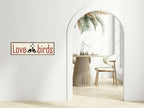 Arch-shaped mirror reflecting a dining area with a 'Love Birds' sign on the wall.