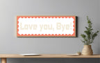 Decorative sign with 'Love you, Bye!' text on a wall above a wooden table.
