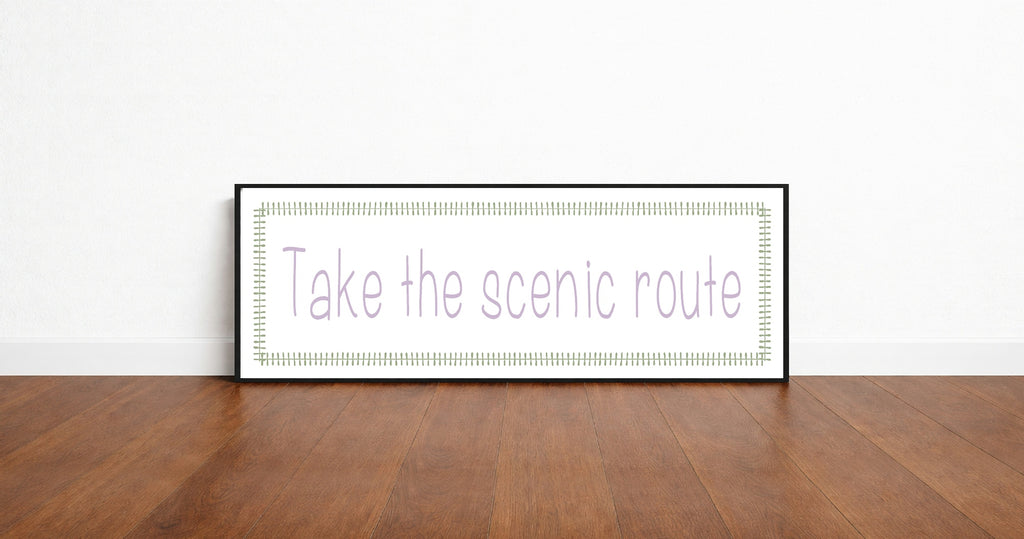 Framed print with 'Take the scenic route' text on a wooden floor and white wall background