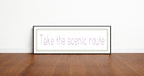 Framed print with 'Take the scenic route' text on a wooden floor and white wall background