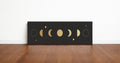Gold moon phases panoramic wall art print in a black frame standing on a wooden floor