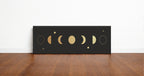 Gold moon phases panoramic wall art print in a black frame standing on a wooden floor