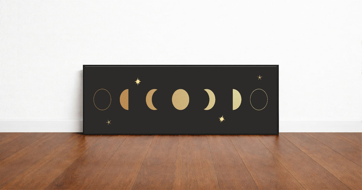 Gold moon phases panoramic wall art print in a black frame standing on a wooden floor